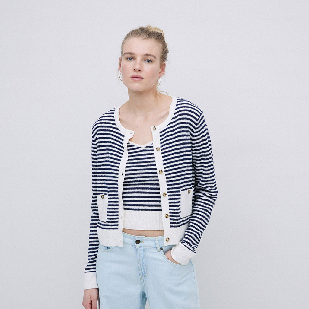 A woman wearing a navy and white stripped cardigan white white edges, two front pockets and round neckline. 