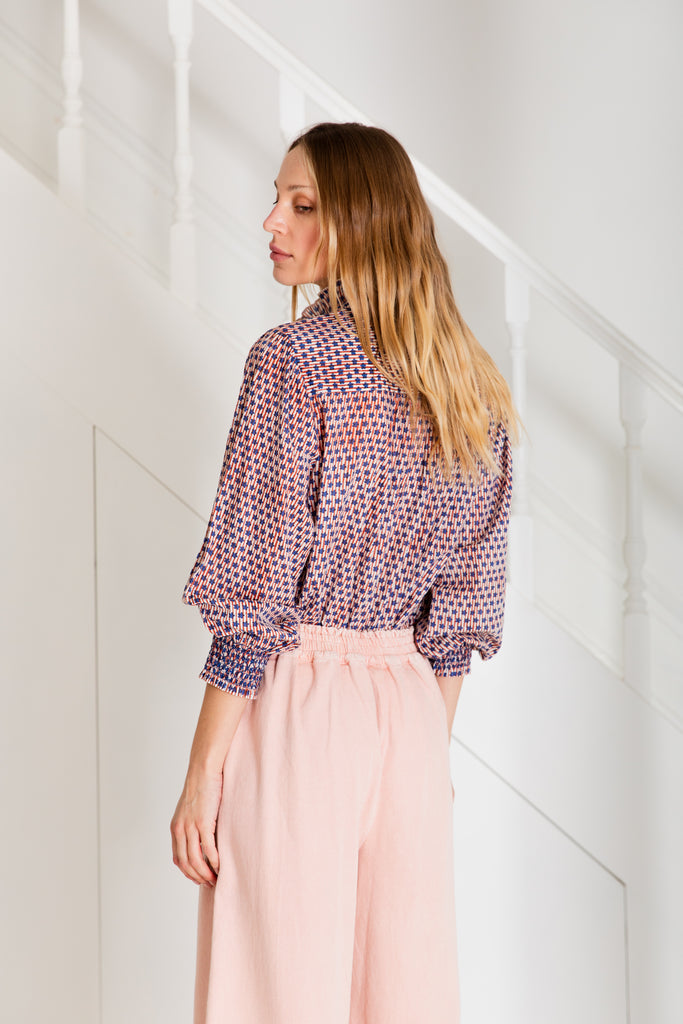 A woman with long hair wearing a patterned shirt in purple and orange, paired with light pink pants by Bonte.