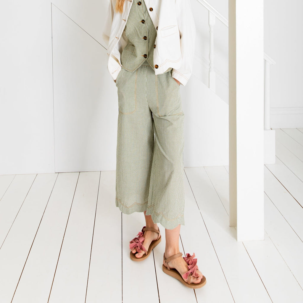 A person in a green checked jumpsuit and a white jacket, wearing Bonte sandals with pink bows.