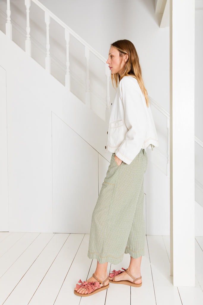 Woman in Bonte clothing, wearing a white jacket and green patterned pants, with pink sandals, standing by stairs.