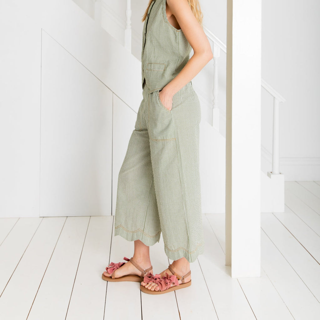 A model in a green checkered outfit by Bonte and pink ruffled sandals, standing near a white staircase.