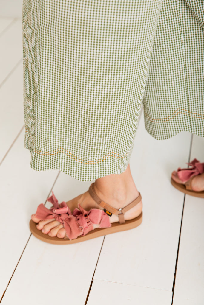 A close-up of a foot wearing Bonte sandals with pink fabric ruffles, paired with green checkered pants.