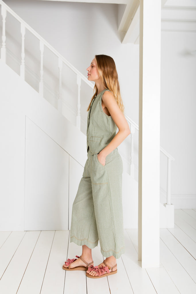 A woman wears a green and white checkered outfit by Bonte, paired with pink sandals, standing near white stairs.