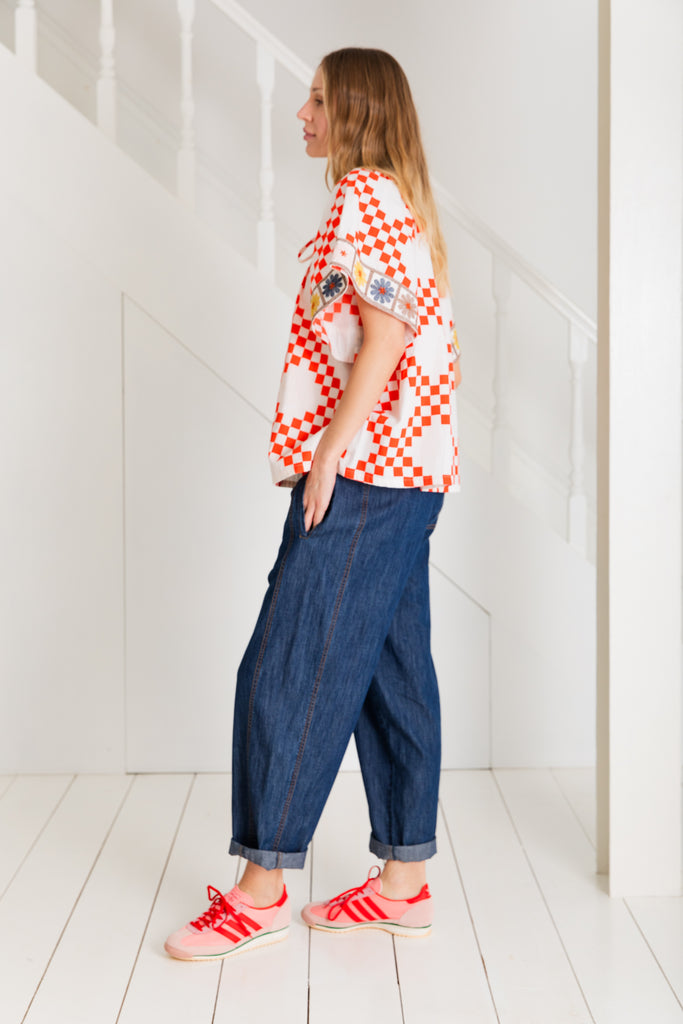 A woman in a red and white checkered top and dark denim pants, wearing pink sneakers by Bonte.