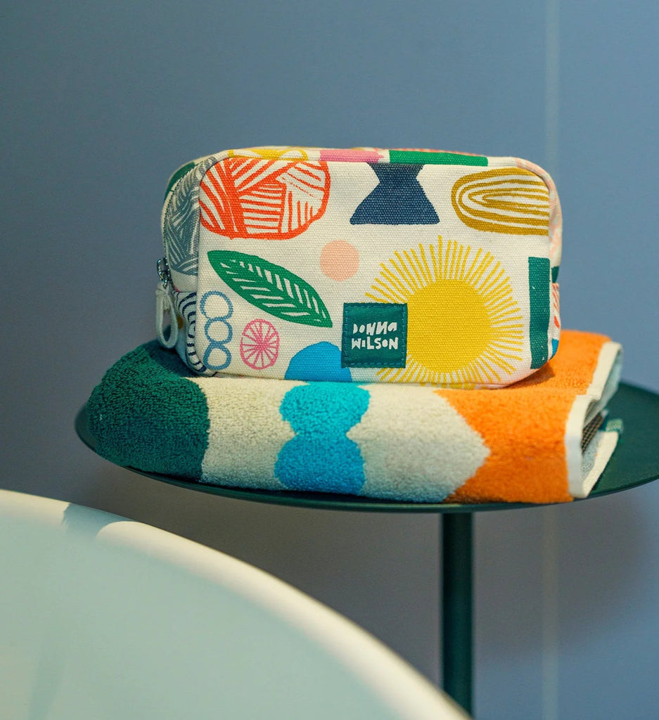 Colorful Donna Wilson pouch on green and orange towels, featuring pink, yellow, blue, and green patterns.