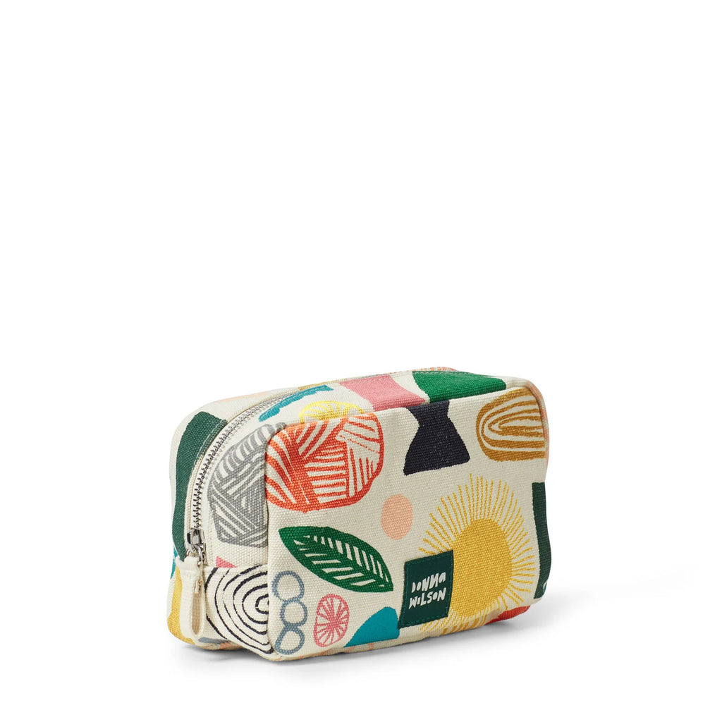 A colorful Donna Wilson pouch featuring green, red, yellow, black, pink, and gray patterns on a cream background.