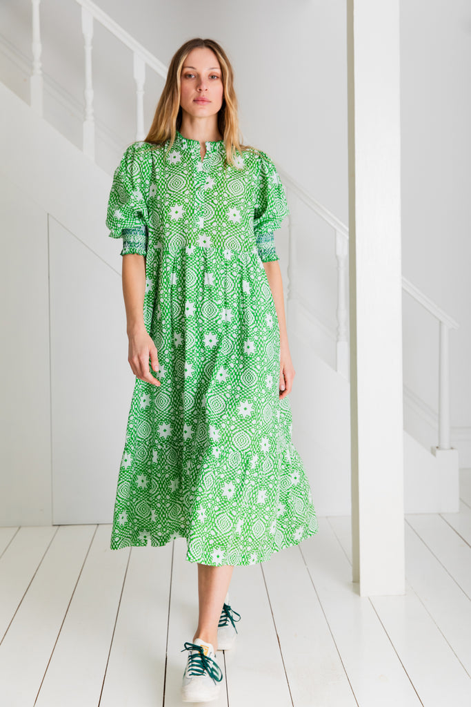 A woman models a green patterned dress by Bonte, featuring white designs and paired with green and white sneakers.