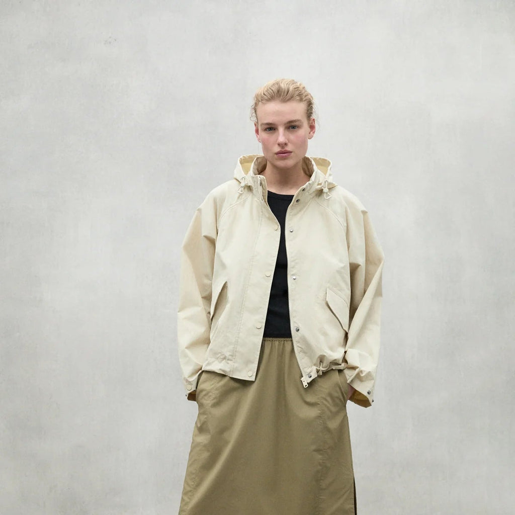 A model wears a beige Ecoalf jacket over a black top and a khaki skirt against a neutral background.