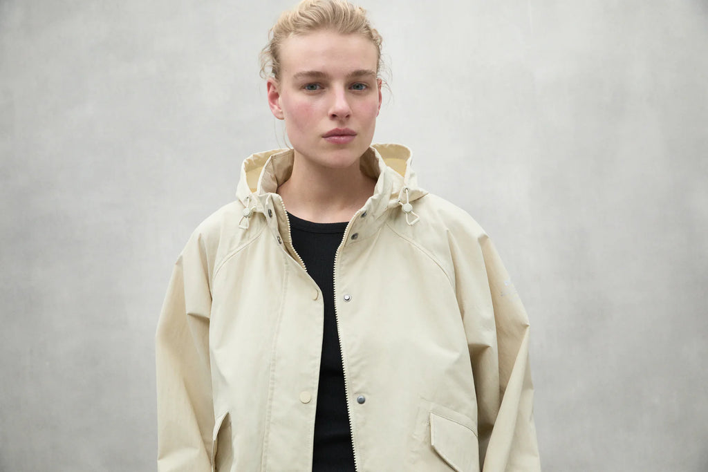 A model wears a light beige Ecoalf jacket over a black shirt, standing against a neutral background.