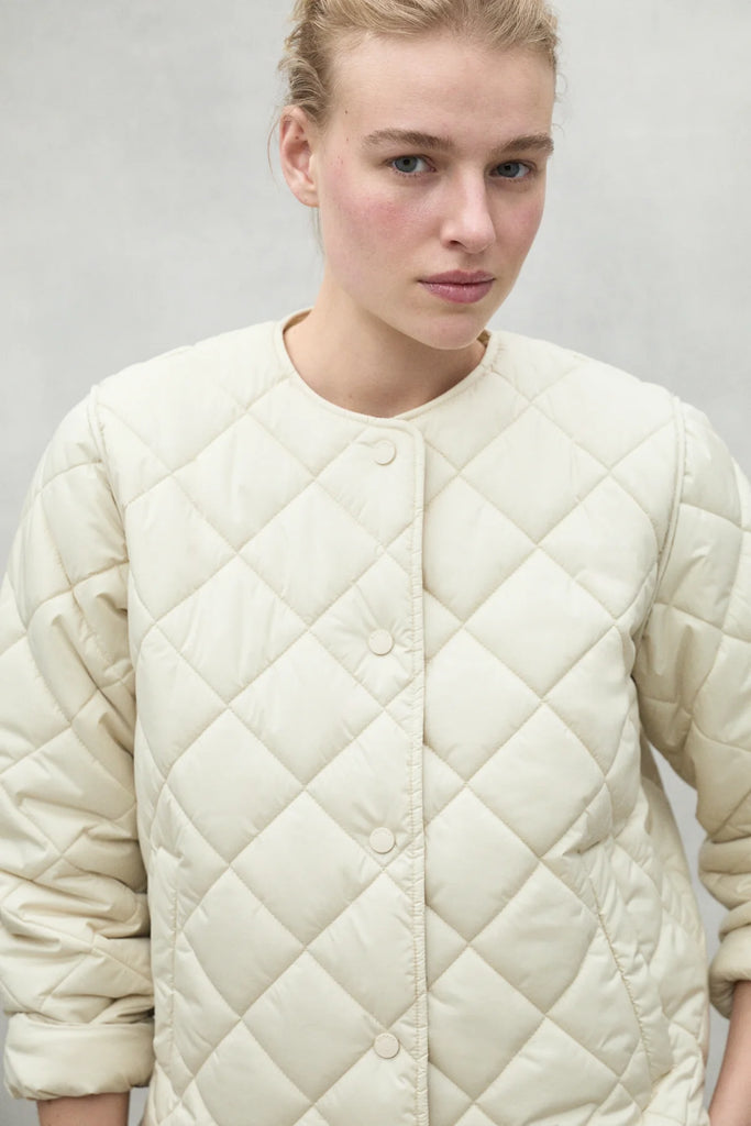 A model wearing a light beige Ecoalf quilted jacket, featuring diamond patterns and a round neckline.