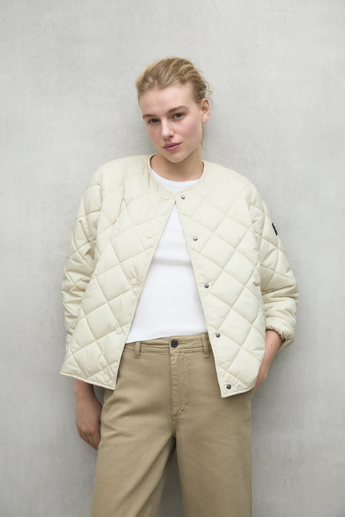 Model wearing an Ecoalf cream quilted jacket over a white shirt and beige pants against a concrete background.