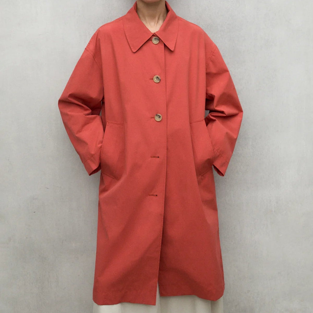 A person in a coral Ecoalf coat with buttons, standing against a neutral background.