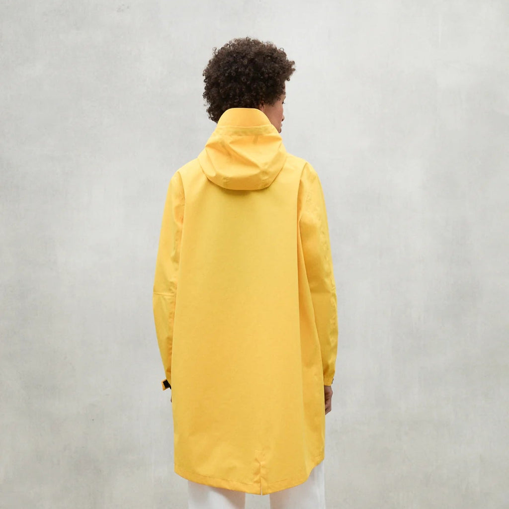 A person wearing a long yellow Ecoalf raincoat stands with their back to the camera against a neutral background.