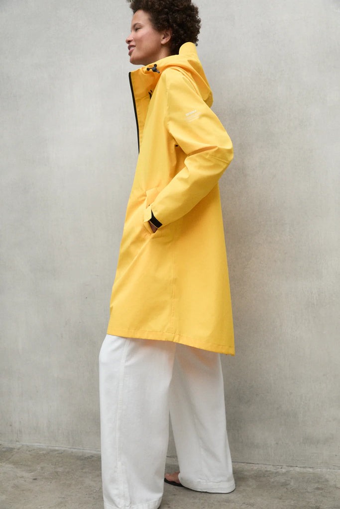 Model wearing a bright yellow Ecoalf jacket and white wide-leg pants, smiling against a gray background.