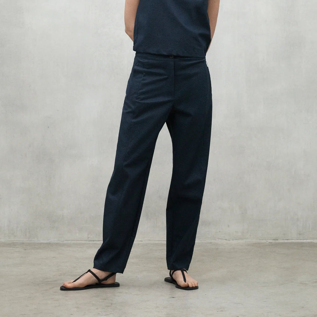 Model wearing a dark blue Ecoalf top and trousers, paired with black flip-flops, in a minimalist setting.