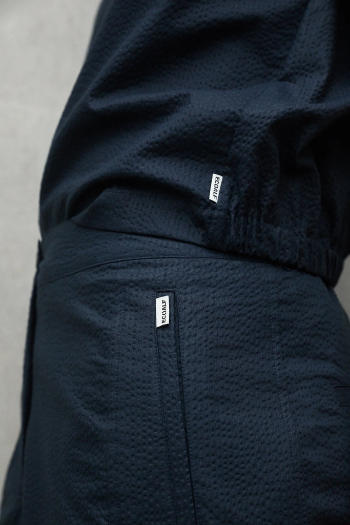 Close-up of dark navy Ecoalf clothing with textured fabric and brand tags visible on the waistband and pockets.