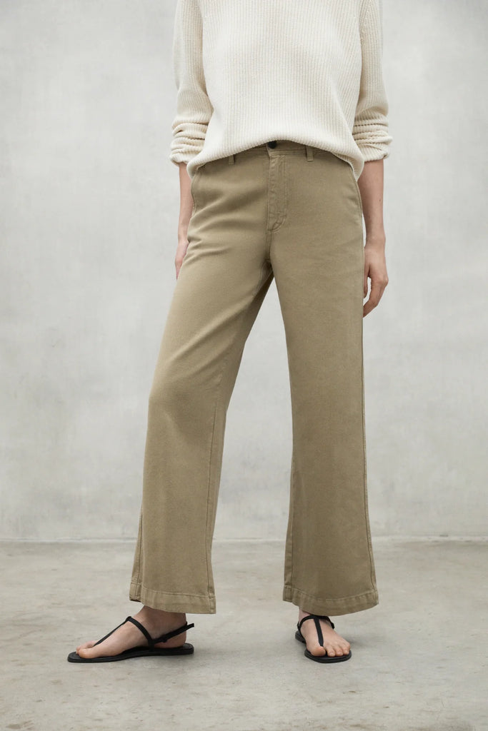 Model wearing Ecoalf beige wide-leg trousers and a cream sweater, paired with black flip-flops, set against a gray backdrop.