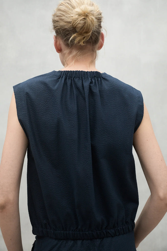 A person seen from behind wearing a navy Ecoalf top with a gathered neckline and short sleeves.