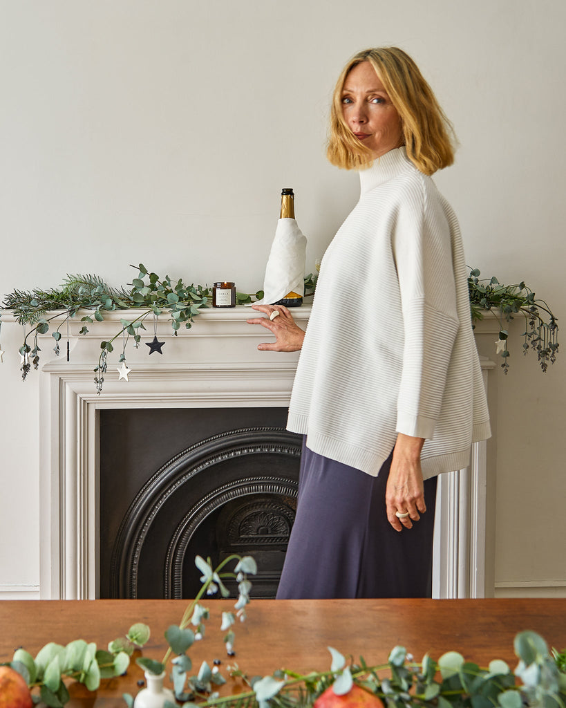 A woman in a white top and navy skirt stands by a decorated mantel, showcasing Chalk UK's chic style.