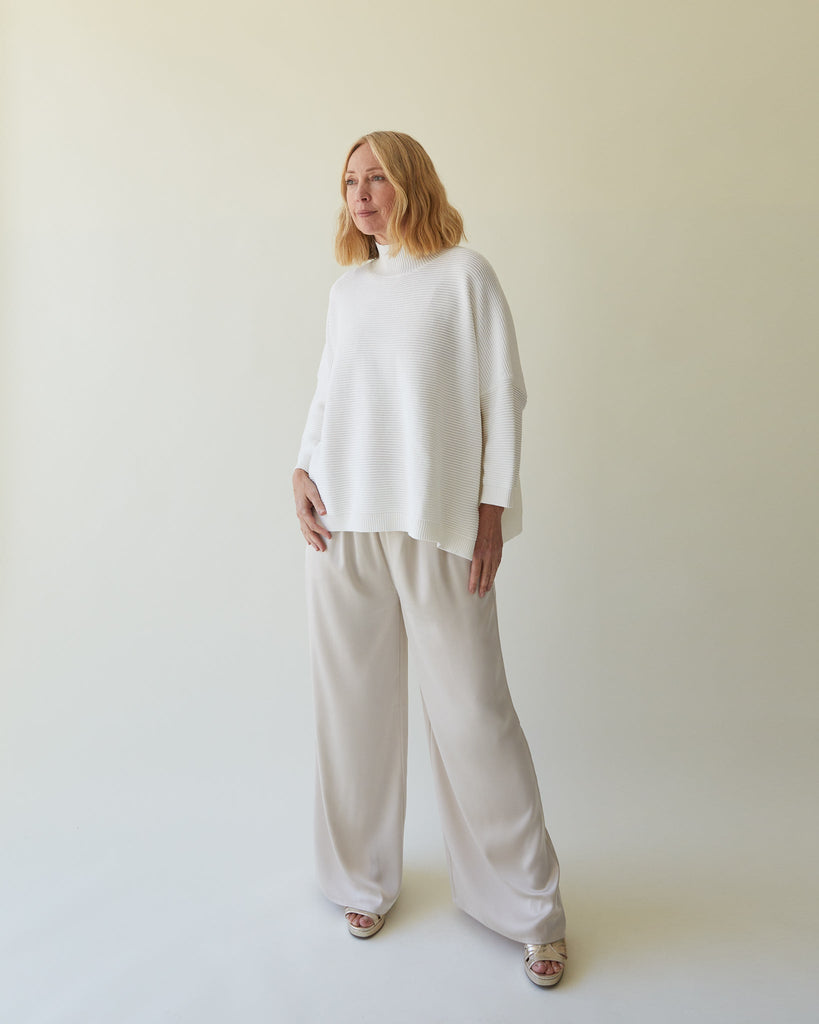 A woman models Chalk UK clothing, wearing a white top and light beige trousers, against a soft background.