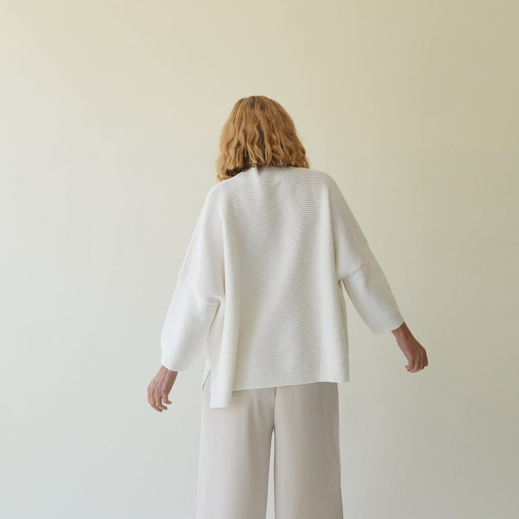 Model wearing Chalk UK in a white oversized sweater and light beige wide-leg trousers, facing away from the camera.