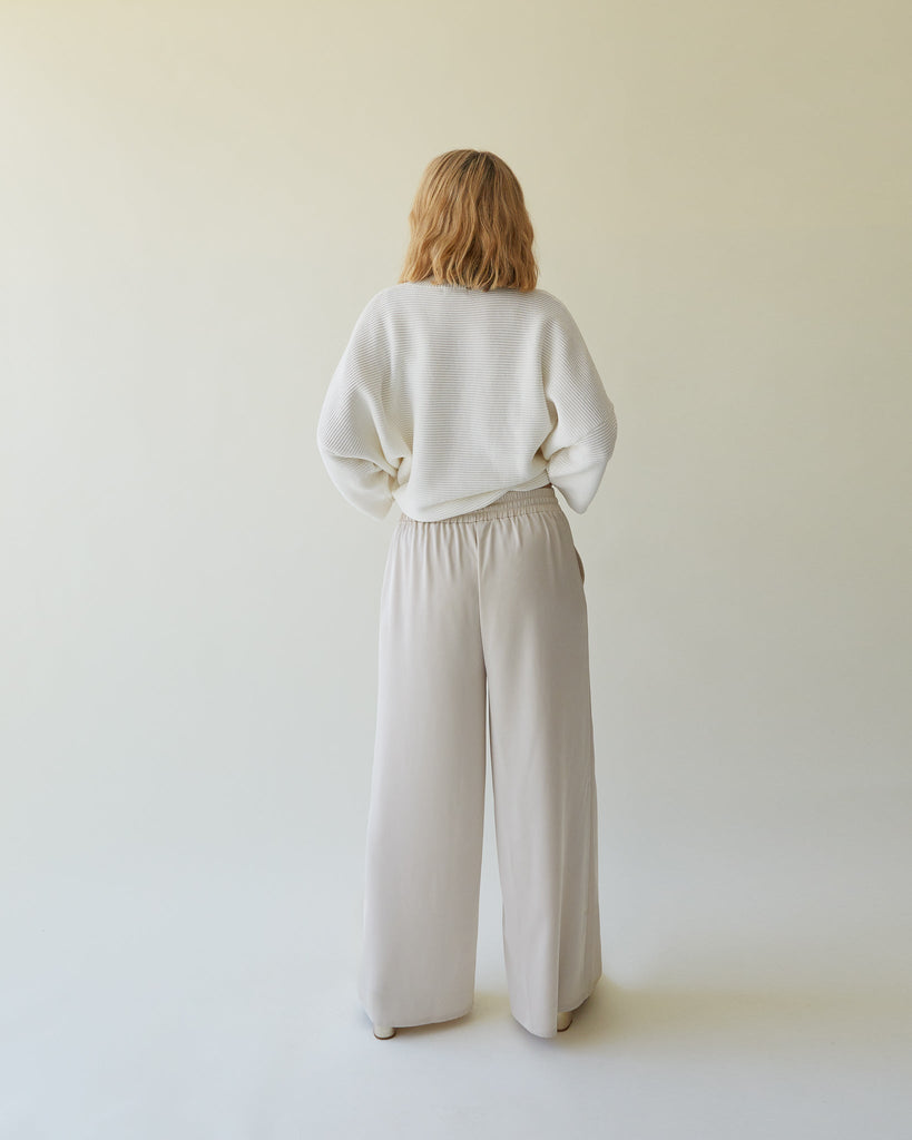 A woman in a white sweater and beige wide-leg pants, showcasing Chalk UK fashion from the back.