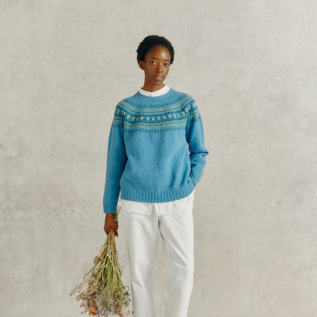 a female model holding a bunch of dried flowers, wearing white linen trousers and a Harley of Scotland Fairisle Jumper - Coll